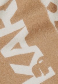Weiche Woll-Decke in Braun und Creme mit einem auffälligen geometrischen Muster. Die Textur wirkt samtig, mit sichtbaren Fasern und sauberen Kanten.