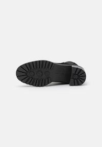 Suela de goma negra con un patrón de relieve profundo. El zapato tiene unupper texturizado, con acentos de ante y detalles de costura a lo largo de los lados.