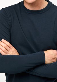 Marineblå longsleeve bomulds skjorte med rund hals; glat tekstur, tætsiddende design og kontrastfarvede manchetter synlige.