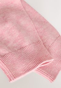 Primer plano de las mangas de un suéter rosa de punto con puños acanalados sobre un fondo claro.