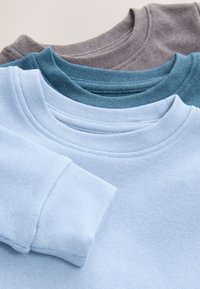 Drei gefaltete Rundhalspullover in Hellblau, Türkis und Grau, gestapelt, wobei der hellblaue Pullover oben liegt und seine Manschette zeigt.