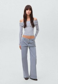 Siva off-shoulder dolgi rokav vrh v kombinaciji s širokimi sivimi džins hlačami. Opozoriti je mogoče na rebrasto teksturo in gumbe kot poudarek na denimu.