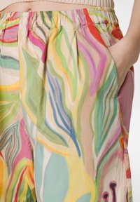 Pantaloni colorati e con fantasia caratterizzati da una miscela di spirali rosa, verdi e gialle, realizzati in tessuto leggero, con tasche laterali e cintura elastica.