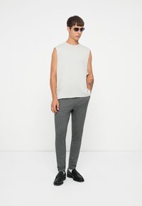 Top sin mangas gris claro, pantalones ajustados de cuadros grises, mocasines negros y gafas de sol oscuras. Diseño minimalista con un aspecto moderno.
