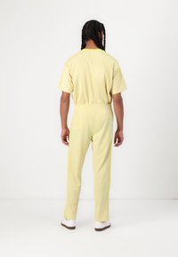 Chándal deportivo amarillo con mangas cortas, cinturilla elástica y franjas laterales amarillas en contraste. El material parece suave y ligero.