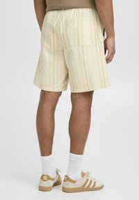 Pantalones cortos a rayas de color amarillo claro con un corte relajado, cinturilla elástica y un bolsillo trasero. Combinados con calcetas blancas y zapatillas beige.