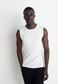 White sleeveless t-shirt, smooth cotton fabric, round neckline, fitted design, paired with black pants, against a plain white background.