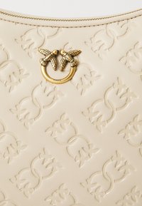 Bežna embosirana usnjena torbica, ki se ponaša z značilnim zlatim kovinskim okrasjem z dvema pticama in zadrgo na vrhu.