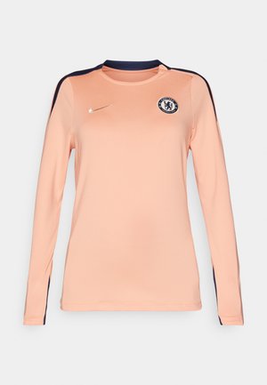 Dugi rukav dres u svijetlo breskvastoj boji s tamnoplavim detaljima, s okruglim izrezom, Nike logotipom i Chelsea FC grbom na prsima.