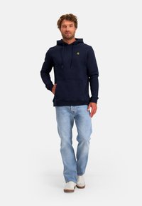 Marineblauwe hoodie van een katoenmix, met een voorzak, een capuchon met trekkoord en een klein logo op de borst. Draagt bij lichte jeans.