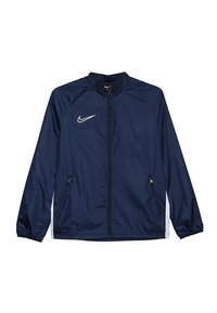 Námořnická Nike bunda s předním zipem, stojáčkovým límcem, elastickými manžetami a bočními kapsami; obsahuje bílé logo a kontrastní bílé akcenty.