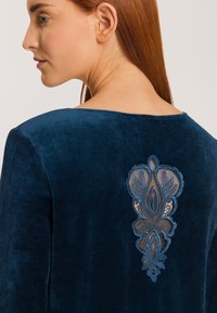 Mörkblå sammetsplagg med en detaljerad spetsapplikation på baksidan, som visar upp intrikata blommönster och ett genomskinligt panel.