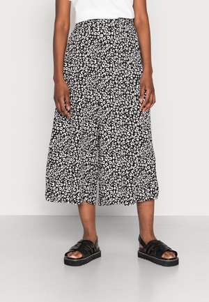 Culottes imprimées en noir et blanc avec une coupe ample, présentant un motif de taches léopard et une taille élastique ; portées avec des sandales noires à brides.