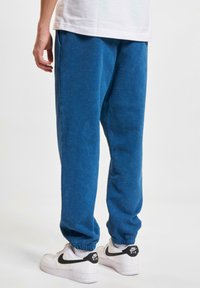 Blue fleece jogger pants with elastic cuffs, side pockets, and a soft texture. Paired with white Nike sneakers featuring black accents.