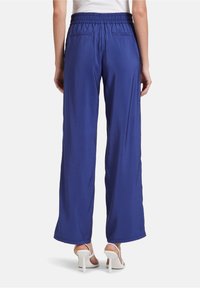 Breda blå byxor med en slät textur, elastisk midja och två bakfickor. Bärs med vita sandaler med remmar.