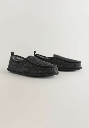 Zwarte gebreide slippers met een zachte interieurvoering, flexibele zool en ronde neus. Voorzien van trektabs voor eenvoudig aan- en uittrekken.