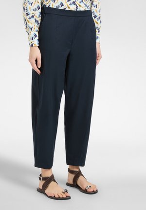 Person iført navyblå smalle bukser, mønstret langærmet skjorte og brune åbne sandaler med ankelremme.