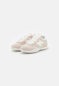 Lightweight athletic sneakers made of cream and light pink suede, featuring white laces, a textured sole, and a subtle logo detail.