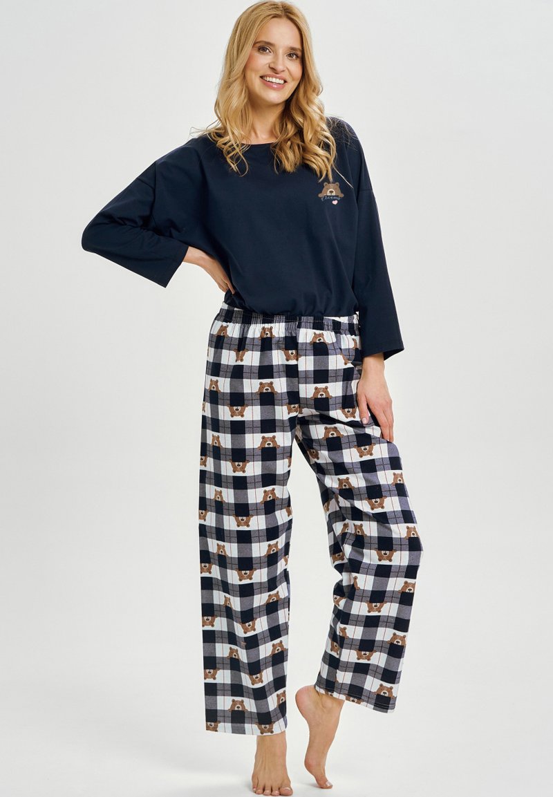 Granatowa bluzka z długim rękawem z nadrukiem niedźwiedzia, zestawiona z flanelowymi spodniami do piżamy w kratę z motywem niedźwiedzi w kolorach brązowym, granatowym i białym. Miękki materiał.