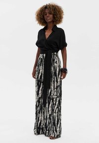 Zwarte wikkeltop gecombineerd met een hooggetailleerde, gemusterde zwart-witte maxirok. De rok heeft een gestrikte riem en een soepelvallende stof.