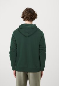 Sudadera de color verde oscuro hecha de una tela suave, con capucha ajustable, puños acanalados y un corte relajado. Sin patrones ni logotipos visibles.