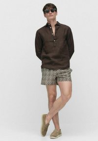 Bruine linnen overhemd met een knoopkraag, gepatternde beige shorts en lichtgekleurde espadrilles, aangevuld met donkere zonnebril.