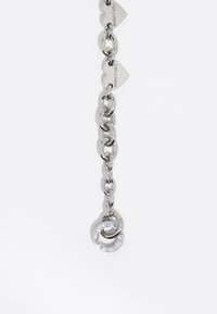 Cadena de metal plateado con eslabones entrelazados, dos etiquetas con forma de corazón y un colgante circular con pequeñas piedras preciosas. Textura suave y pulida.