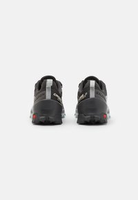 Zapatillas de trail running en negro y gris con material texturizado, lengüetas traseras de tirón y suela de goma durable con prominentes tacos de tracción.
