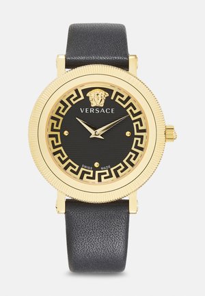 Gold-tone watch with black dial, Greek key pattern, and Versace logo. Leather strap and Swiss-made markings. Round case with textured bezel.