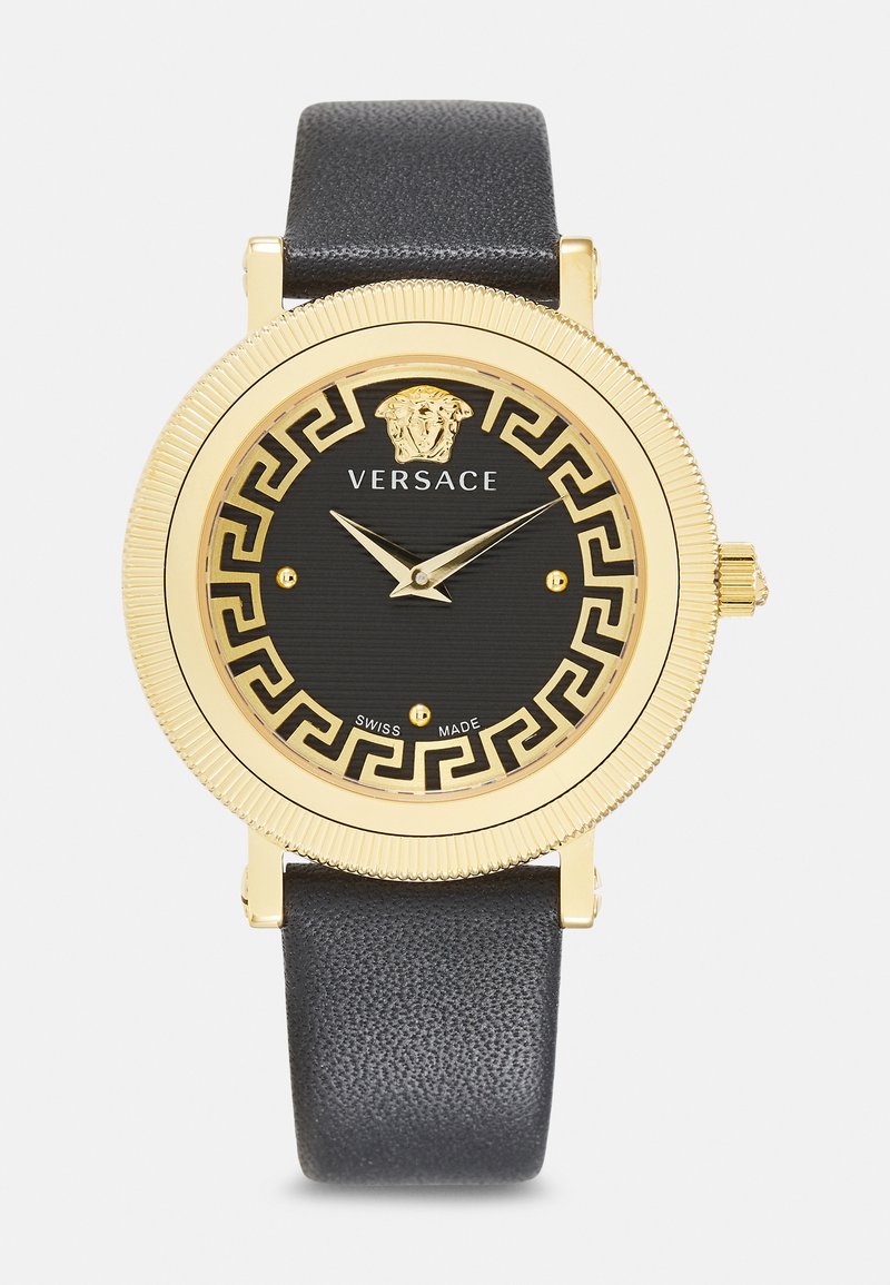 Gold-tone watch with black dial, Greek key pattern, and Versace logo. Leather strap and Swiss-made markings. Round case with textured bezel.