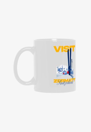 White mug with yellow text "Visit Zermatt Switzerland" beside blue skis and poles over a snowy village scene.