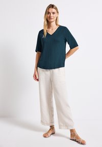 Tyrkysový top s výstřihem do V a krátkým rukávem, kombinovaný s krémovými širokými kalhotami a stříbrnými sandály na pásku. Měkká textura, uvolněný střih.