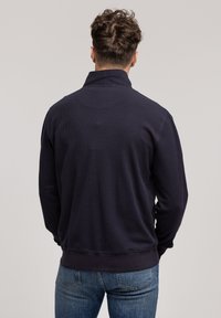 Granatowy pulower z fakturowanym wzorem, wysokim kołnierzem i ściągaczami na rękawach; zestawiony z jasnoniebieskimi dżinsami.