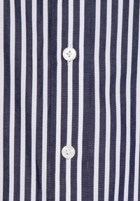 Gros plan sur une chemise à rayures verticales bleu marine et blanches, avec deux boutons blancs au centre.