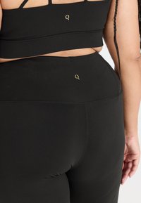 Zwart sporttop en hoge taille leggings van rekbaar materiaal. Kenmerkt zich door een klein gouden logo op de achterkant van elk stuk.