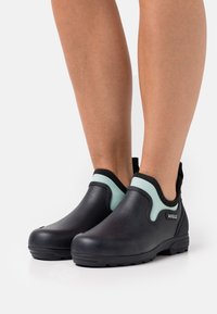 Black rubber ankle boots with a mint-green accent, featuring a smooth texture, elastic side panels, and a textured sole for grip.