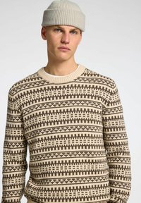 Maglione lavorato a maglia in crema e marrone, con un motivo geometrico, colletto rotondo e polsini a costine. Texture in misto cotone.