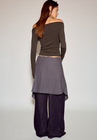 Ciemnobrązowa bluzka z długim rękawem i odkrytymi ramionami, wzorzysta spódnica kopertowa w czarno-białą kratę, szerokie spodnie z ciemnego denimu.