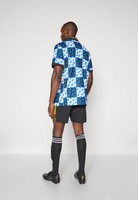 Kortærmet blå mønstret skjorte med sorte kanter, parret med sorte shorts, sorte sokker med hvide striber og sorte fodboldstøvler.