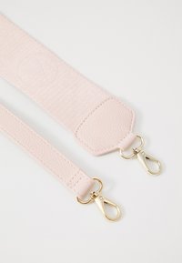 Bandoulières rose clair avec des extrémités texturées et des mousquetons en métal doré sur un fond blanc.