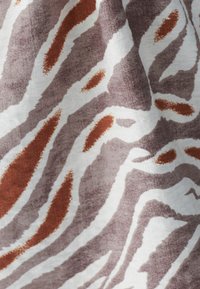 Bomuldsstof med et kraftigt, abstrakt zebramønster i nuancer af brunt og rust mod en lys baggrund med subtil tekstur.