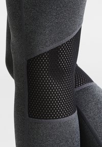 Vysoké sportovní legíny v tmavě šedé barvě, s texturovanými síťovanými panely. Vyrobeny z elastického materiálu s plochými švy.