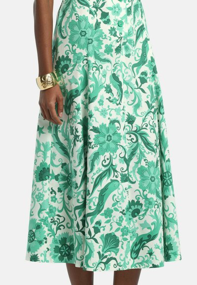 Green and white floral patterned midi skirt with buttons down front, worn with a gold cuff bracelet on left wrist.