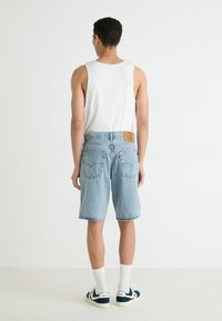 Shorts en denim bleu clair avec une coupe droite, ourlet effiloché et étiquette à l'arrière. Débardeur blanc et baskets bleues avec des chaussettes blanches.