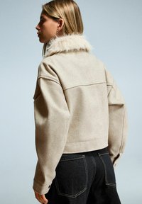 Beige cropped jasje met een zachte bontkraag, gemaakt van een textuur materiaal. Heeft losse mouwen en gestikte naden op de rug.