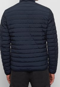 Donkerblauwe gewatteerde jas met een doorgestikt ontwerp, voorzien van een hoge kraag en elastische manchetten. Lichtgewicht materiaal biedt isolatie.