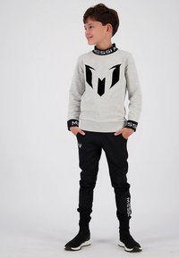 Šedá mikina s černým logem, černé tepláky s bílým nápisem a černé sportovní boty do kotníku. Hladká látka, minimalistický styl.