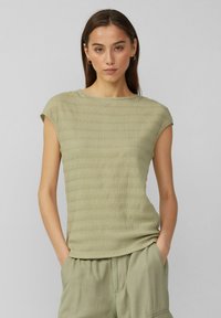 Haut à manches courtes de couleur olive clair avec un design texturé et côtelé. Le matériau semble doux et léger, adapté à un usage décontracté.