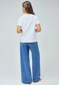 Camiseta blanca de algodón de manga corta, combinada con unos vaqueros de denim azul de tiro alto y corte holgado que cuentan con un diseño clásico de cinco bolsillos y dobladillos deshilachados.