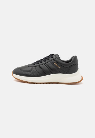 Zapatillas deportivas de cuero negro con una textura suave, que cuentan con tres rayas horizontales, una entresuela blanca y una suela de goma color caramelo. Logo en el costado.